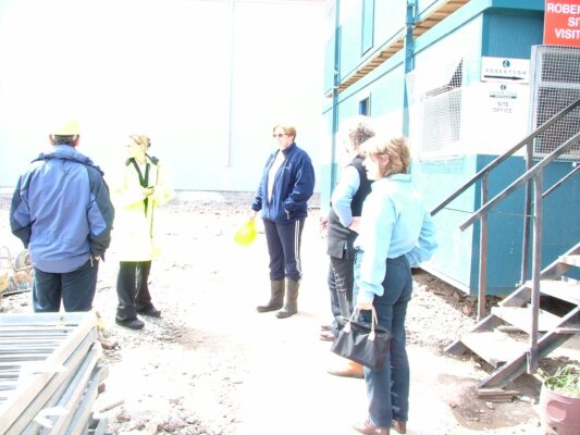 Visitors in hi-vis vests gather outside the Robertson Construction site office ahead of a tour of the new building.