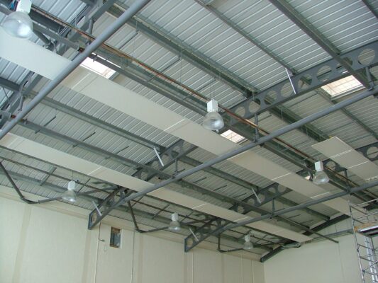 Steel roof trusses crossing overhead, with new light fittings and insulation panels being installed.