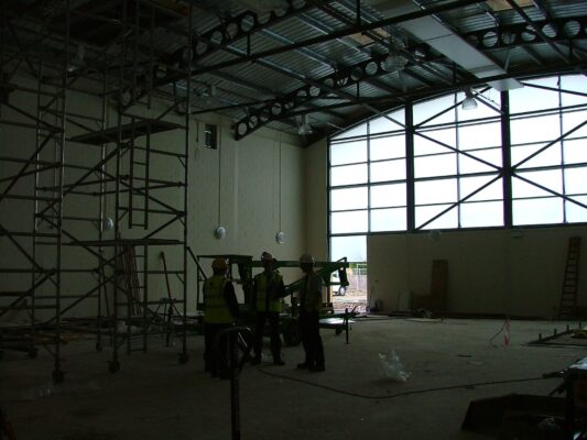 Workers in hard hats silhouetted against the huge arched window that would become the hall's glass gable end.