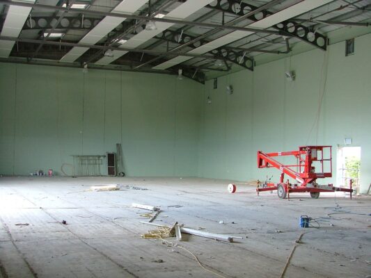 The empty main hall with sage-green painted walls and a bare concrete floor, ready for flooring and equipment.