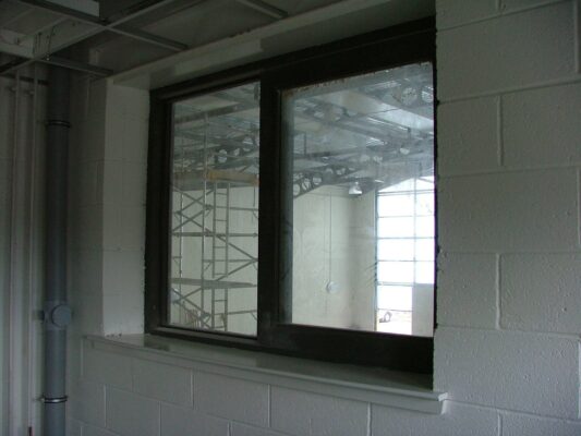 A newly fitted window reflects the scaffolding and ladders inside the hall behind it.