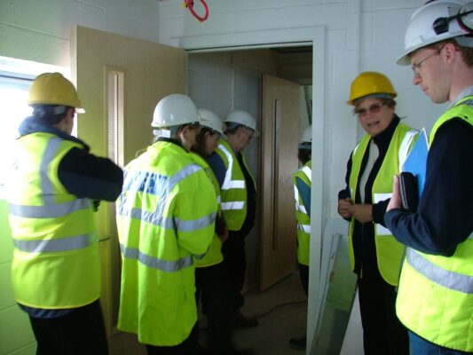 A group of visitors in hard hats and hi-vis vests tour the building's corridors during construction.