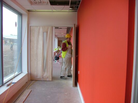 A worker fits a door in the reception corridor, its bold orange feature wall newly painted.