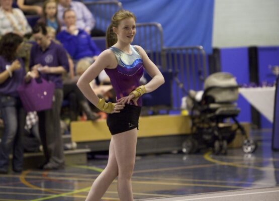 Gymnast in a purple and silver leotard standing with hands on hips as she waits her turn at the 2012 club display
