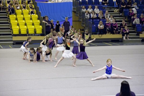 Junior gymnasts in white skirts and purple costumes performing a group floor routine at the 2012 club display