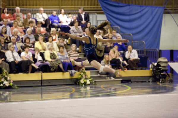 Gymnast performing a split leap high above the floor in front of the audience at the 2012 club display
