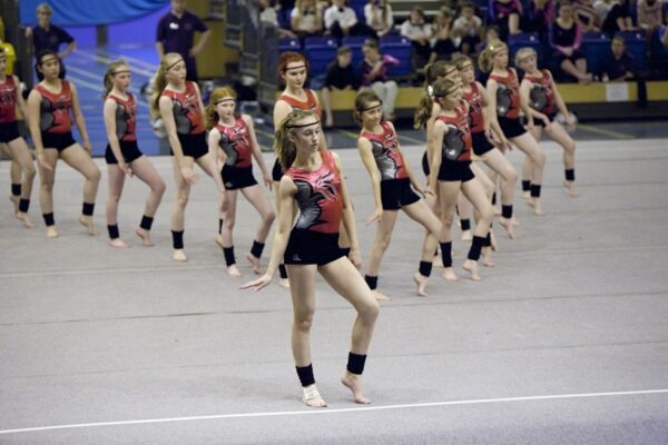 Team of gymnasts in red and black leotards performing a synchronised floor routine at the 2012 club display