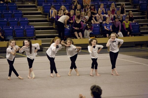 Six young gymnasts in white shirts and bow ties performing a themed dance routine at the 2012 club display