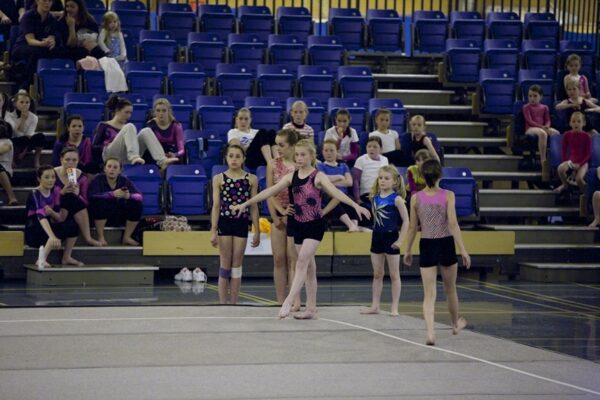 Young gymnasts in colourful leotards waiting on the floor at the Auchterarder Gymnastics Club 2012 display, with spectators in the stands behind