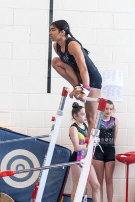 Gymnast perched on top of the bar frame while others watch