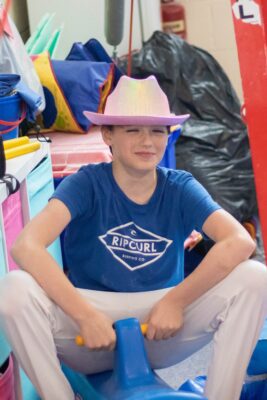 Boy in a pink cowboy hat sitting on gym equipment between turns