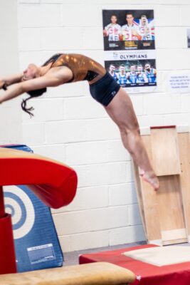 Gymnast arching backwards onto a padded vault trainer