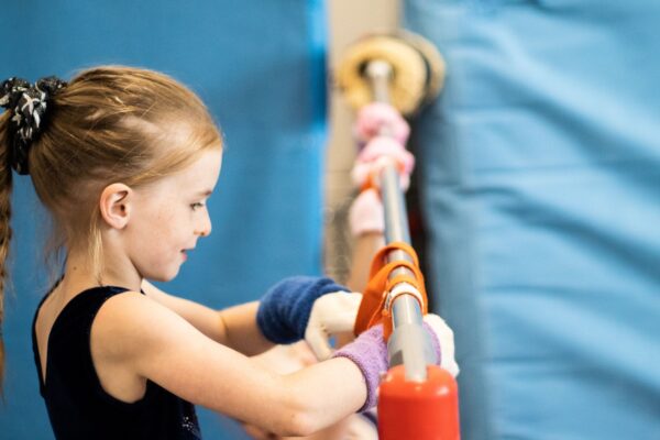 Young gymnast in wrist supports gripping a padded training bar