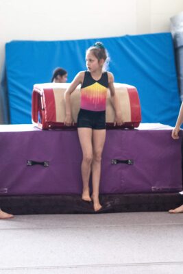 Young gymnast sitting astride a vault trainer between padded mats