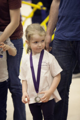Young child in an Auchterarder Gymnastics Club t-shirt wearing a medal on a purple ribbon
